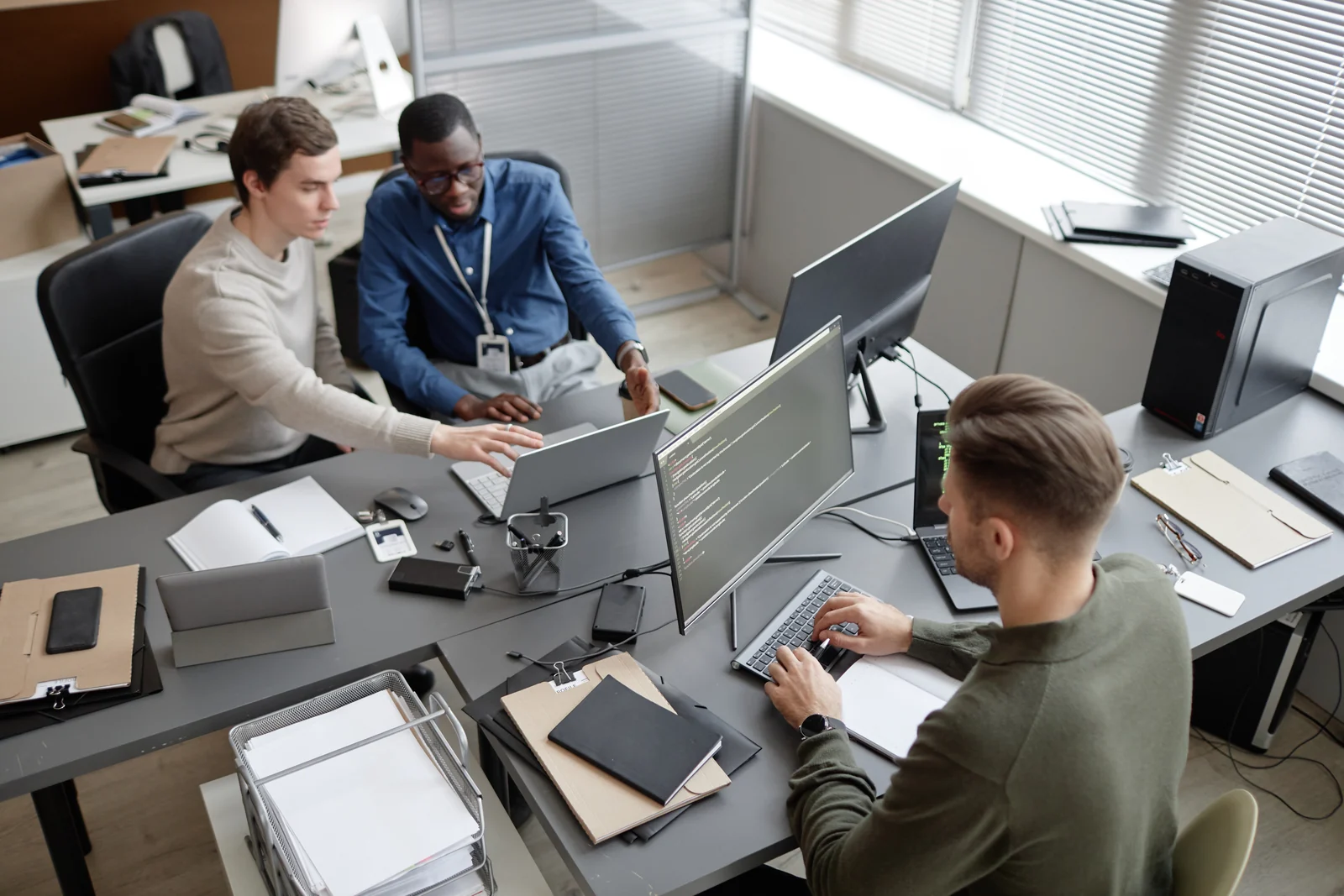 Trois professionnels IT travaillent ensemble sur leurs ordinateurs dans un bureau lumineux.