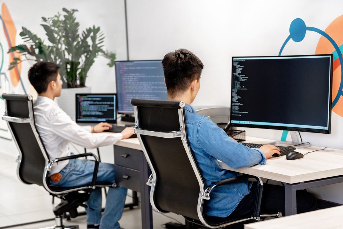 Twee professionals werken aan schermen met code in een licht kantoor.
